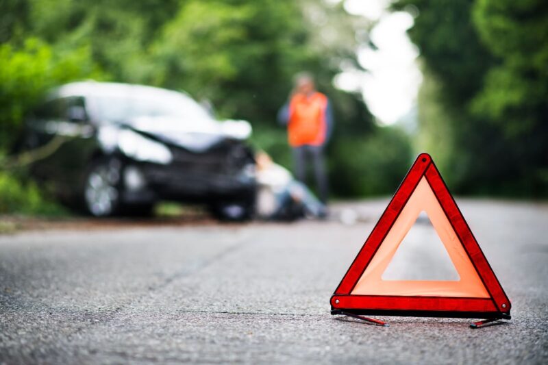 orange triangle hazard sign in foreground with car smashed in background