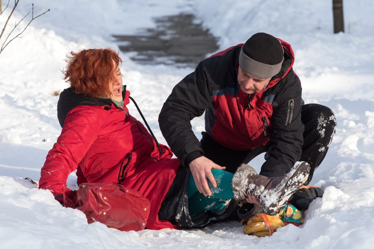 man helping woman in red winter coat down on icy sidewalk