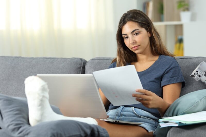 woman with leg is cast sitting on couch looking at paperwork