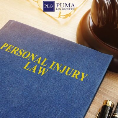 A blue book titled "Personal Injury Law" sits on a desk next to a gavel and pen, with the Puma Law Group logo visible in the background—ideal for anyone seeking a car accident lawyer in Commack.