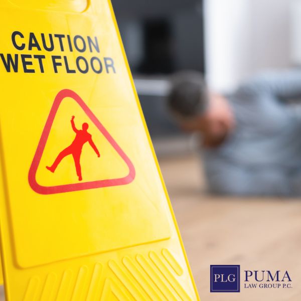Yellow "Caution Wet Floor" sign in focus; person lying on the floor in the background. Puma Law Group logo visible in the corner.