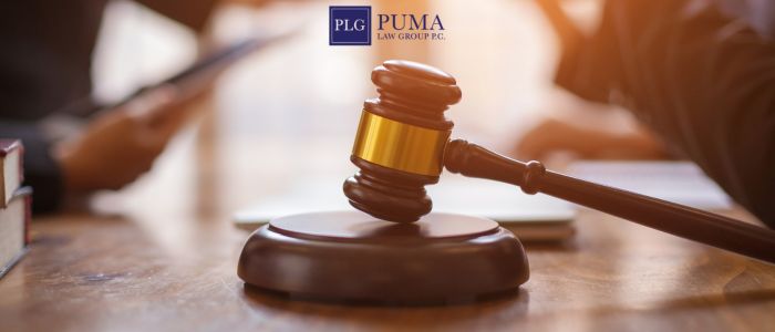 A wooden gavel rests on a table with blurred hands holding documents in the background; the Puma Law Group PC logo appears at the top.