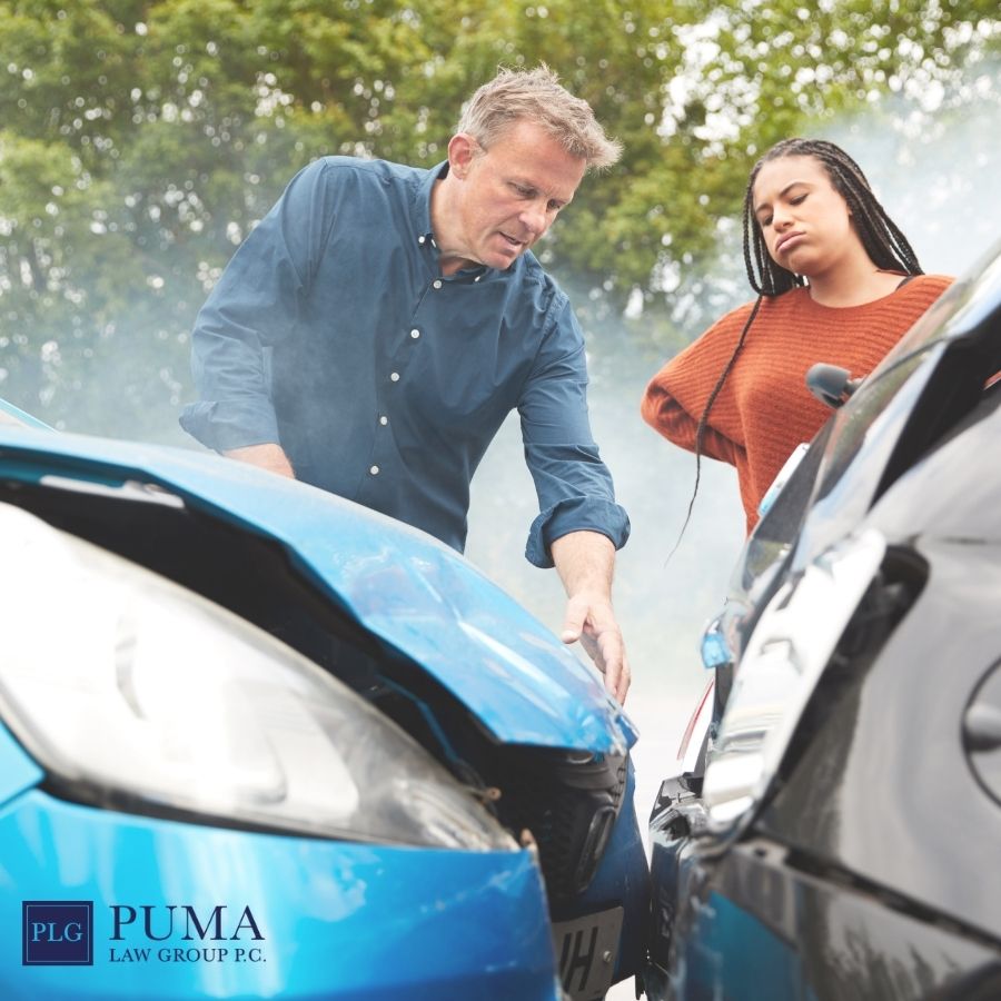 Two people inspect damage to their cars after a collision, smoke visible and both vehicles' front ends crumpled; Puma Law Group logo is present, highlighting the need for a car accident lawyer in Holbrook. Two people inspect damage to their cars after a collision, smoke visible and both vehicles' front ends crumpled; Puma Law Group logo is present, highlighting the need for a car accident lawyer in Holbrook.